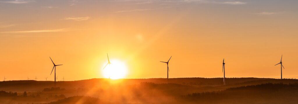 The sun falls behind a row of wind turbines