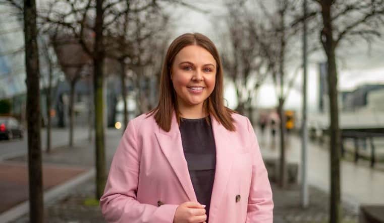 A woman in a stylish pink suit jacket stands on a Dublin street