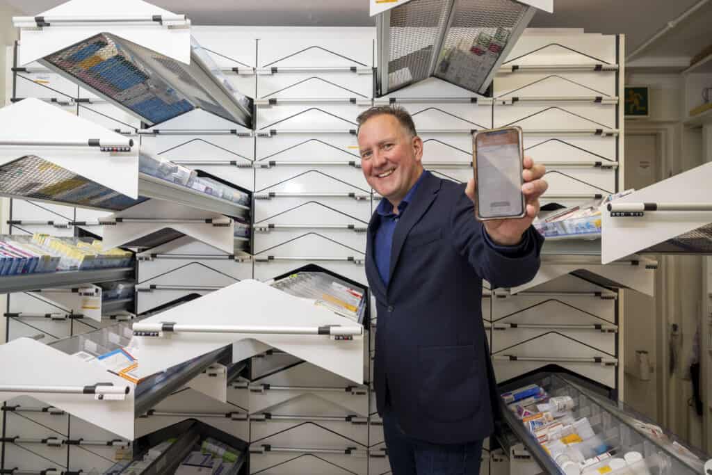 A photograph of Cormac-McKenna the CEO of PharmacyConnect smiles and holds a phone in his hand, suggesting the Online Pharmacy App innovation.