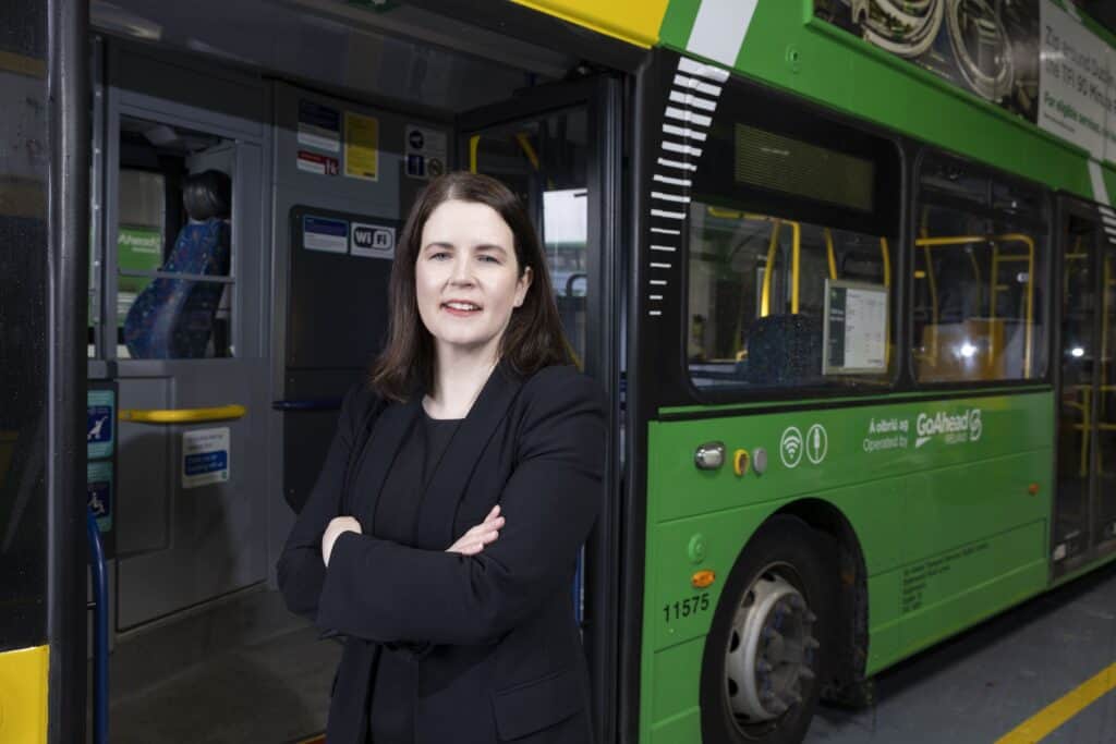 Managing Director of Go-Ahead Ireland, Dervla McKay, standing confidently with arms crossed in front of a Go-Ahead green bus with open doors