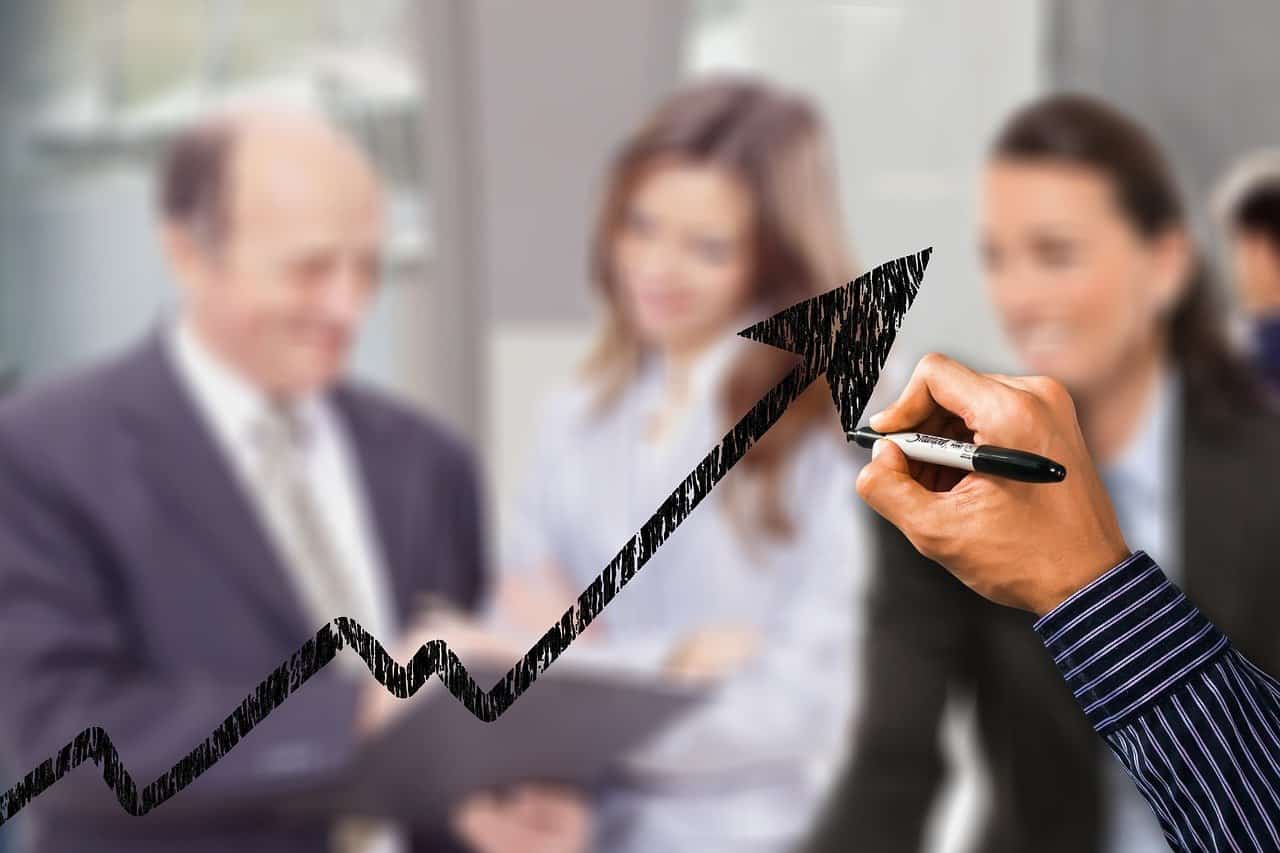 A hand drawing an upward arrow on a transparent surface, representing growth, with blurred figures of professionals in the background.